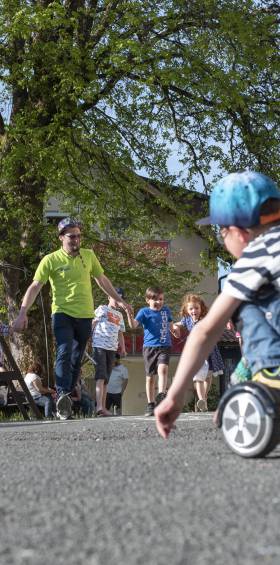 Kinder fahren mit Spielgeräten draußen, Betreuer führt die Gruppe im Familotel Mein Krug