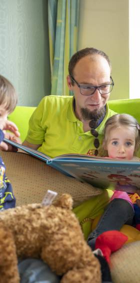 Kinderbetreuer liest zwei Kindern im Spielzimmer eine Geschichte vor