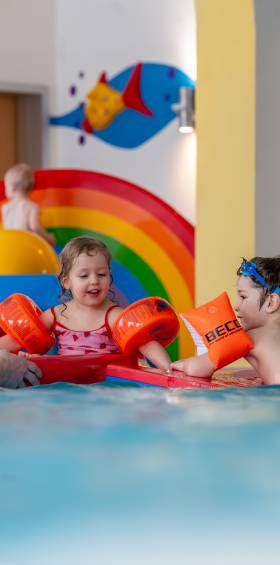 Zwei Kleinkinder mit Schwimmflügeln plantschen im Kinderbecken