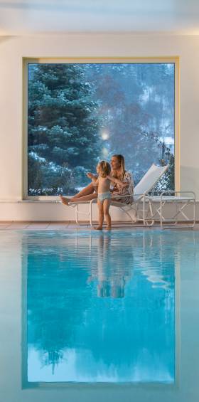 Mutter und Kind sitzend auf Liegestuhl im Indoor-Schwimmbad