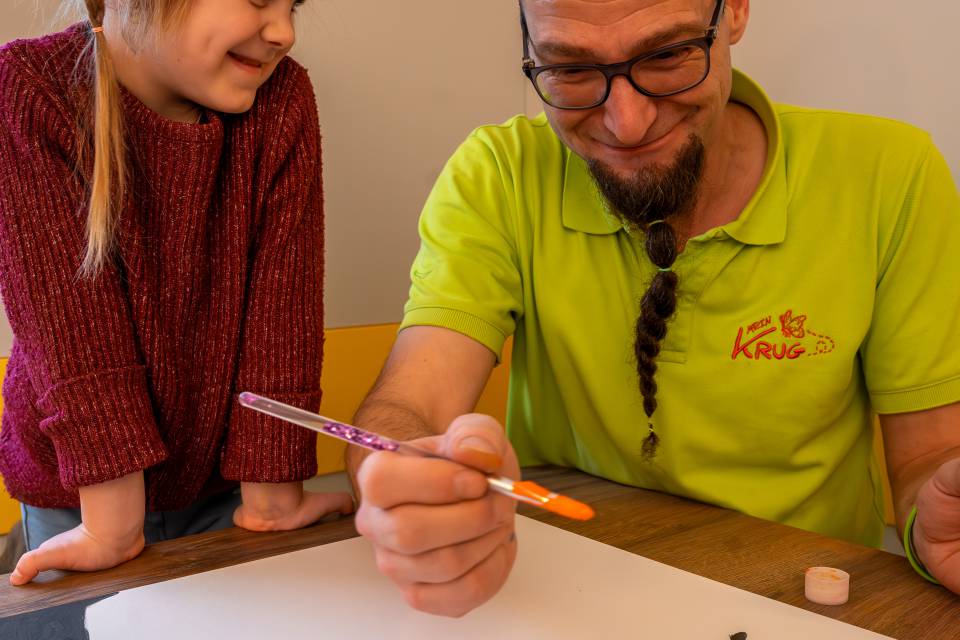 Betreuer und Kind bemalen zusammen eine Leinwand, kreative Aktivität im Familotel