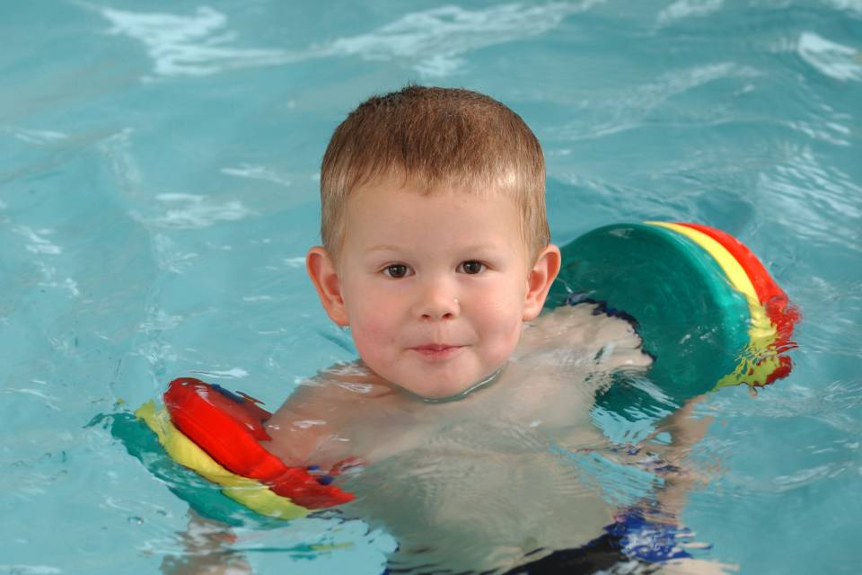 Kleinkind mit Schwimmflügeln planscht fröhlich im Wasser, sicherer Spaß im Familotel Mein Krug