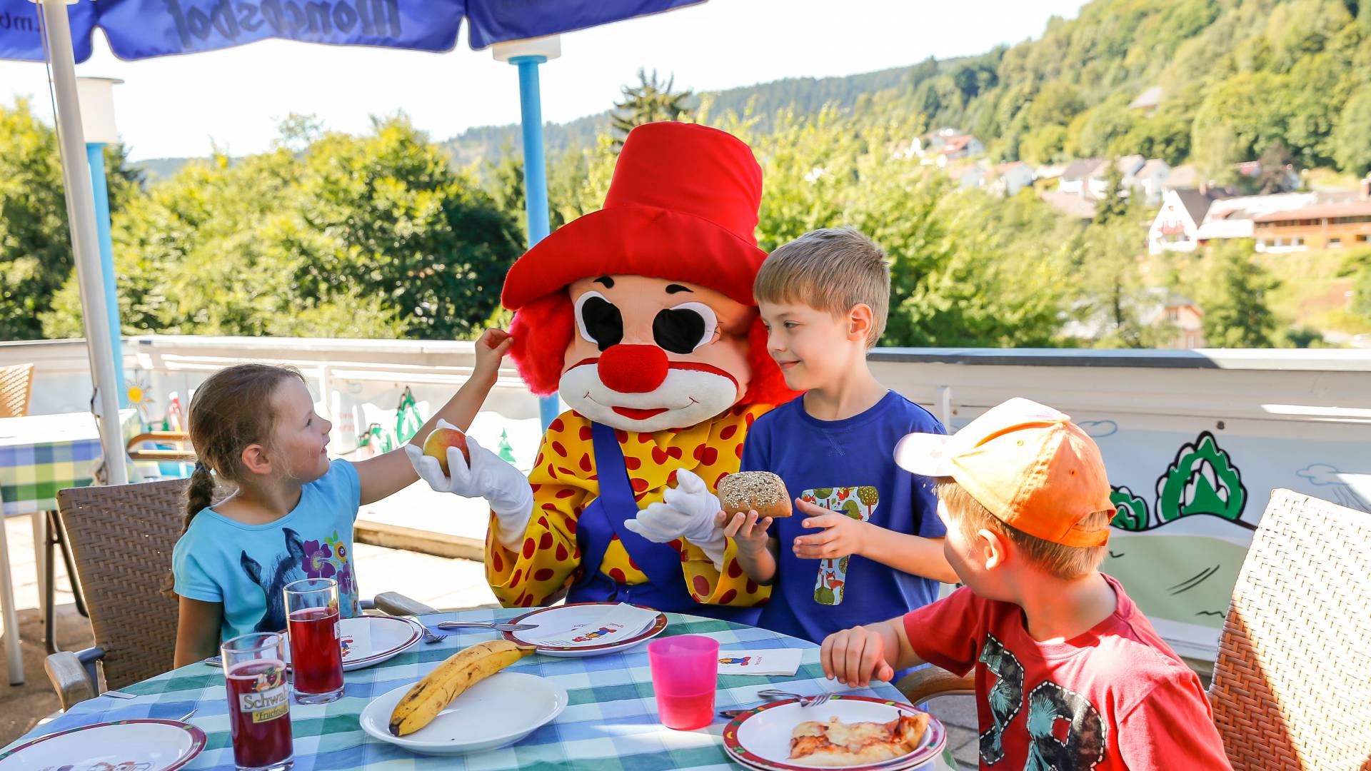 Kinder essen mit Familotel Maskottchen Happy im Freien